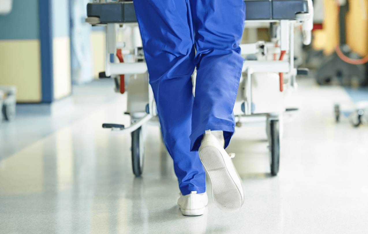 Image of a hospital employee wearing blue scrubs pushing a stretcher down a hallway. 
