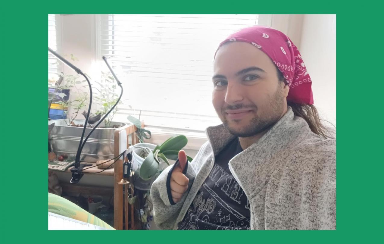 A graduate researcher wearing a bandana and holding up a thumbs up sign looks at the camera