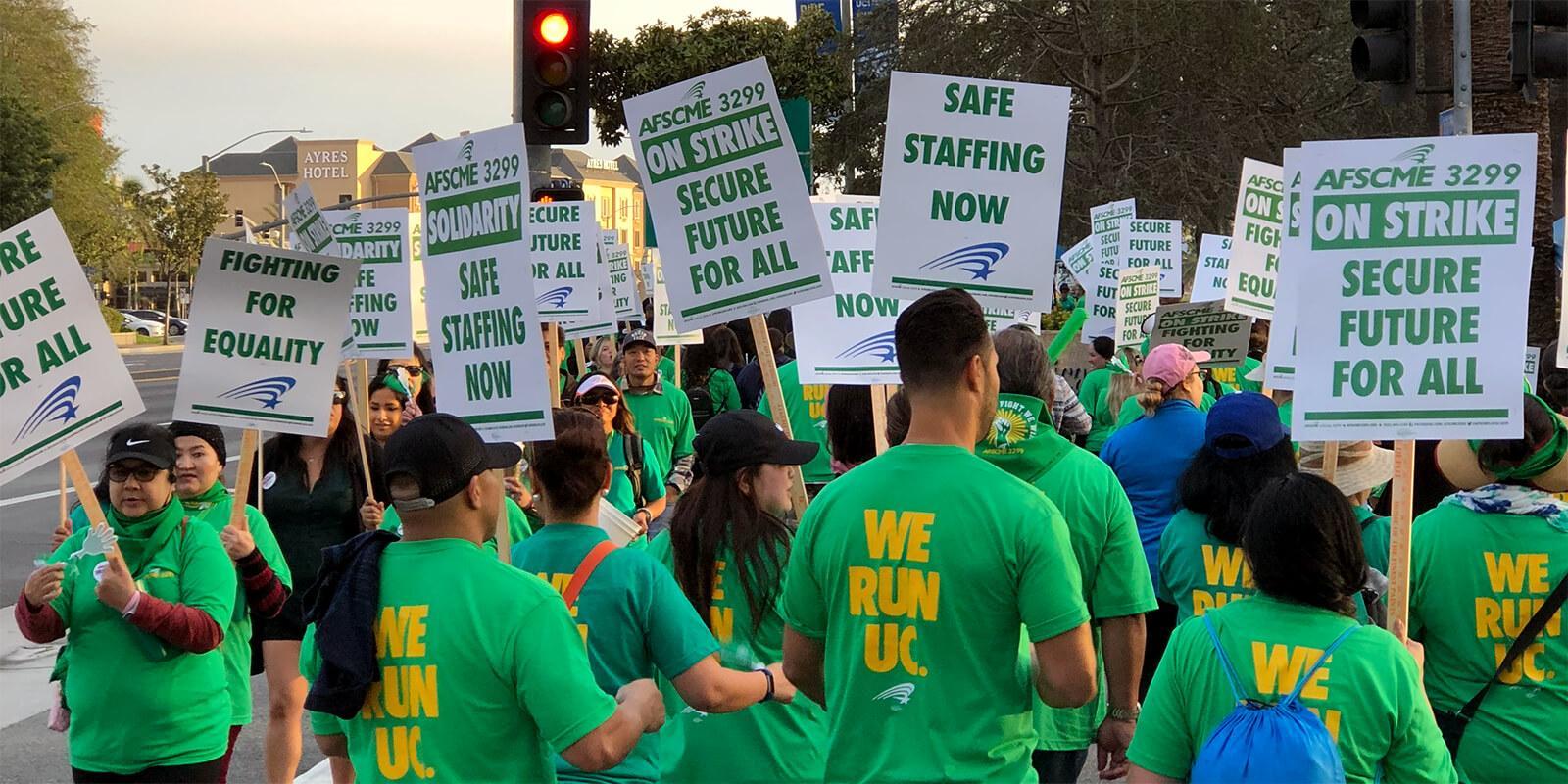 AFSCME 3299 members on the picket line with signs that read, "On Strike, Secure Future For All" and "Safe Staffing Now"