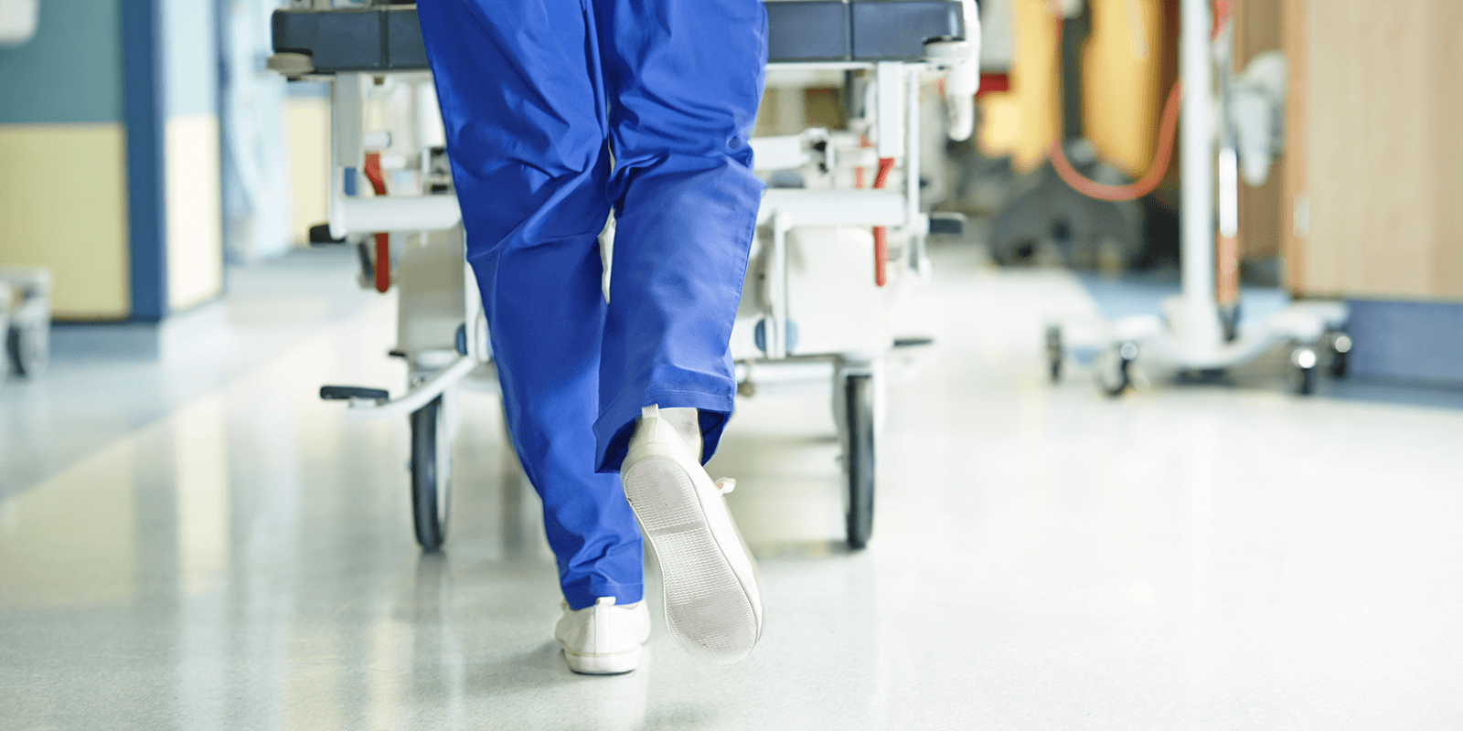 Image of a hospital employee wearing blue scrubs pushing a stretcher down a hallway. 